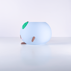 A light blue, rounded, cartoon-like decorative object with small brown legs and a green leaf detail on top, photographed on a clean white studio surface.