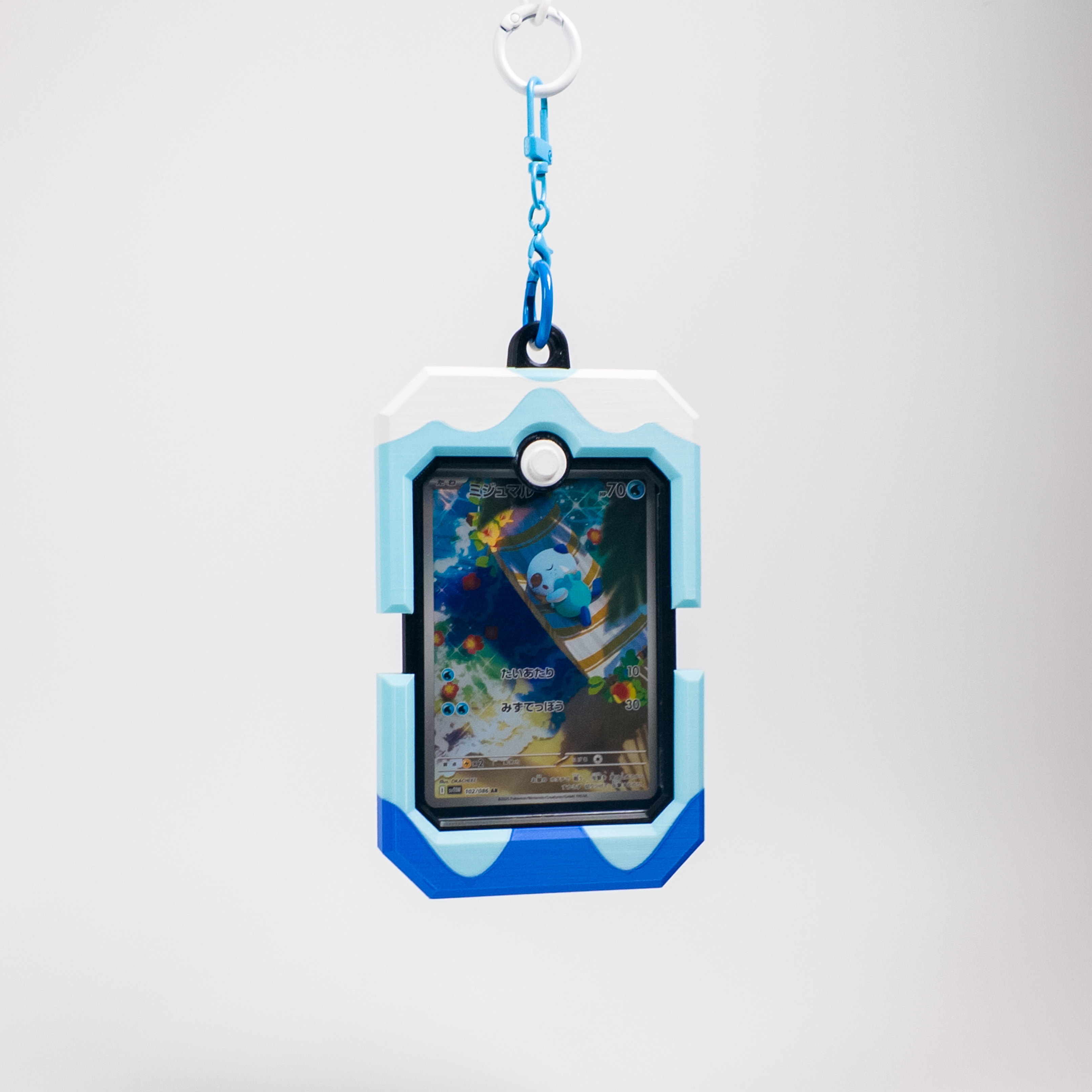 A blue and white rugged protective card holder or game case with a keychain attachment, featuring a screen showing a colorful card illustration, set against a light gray background.