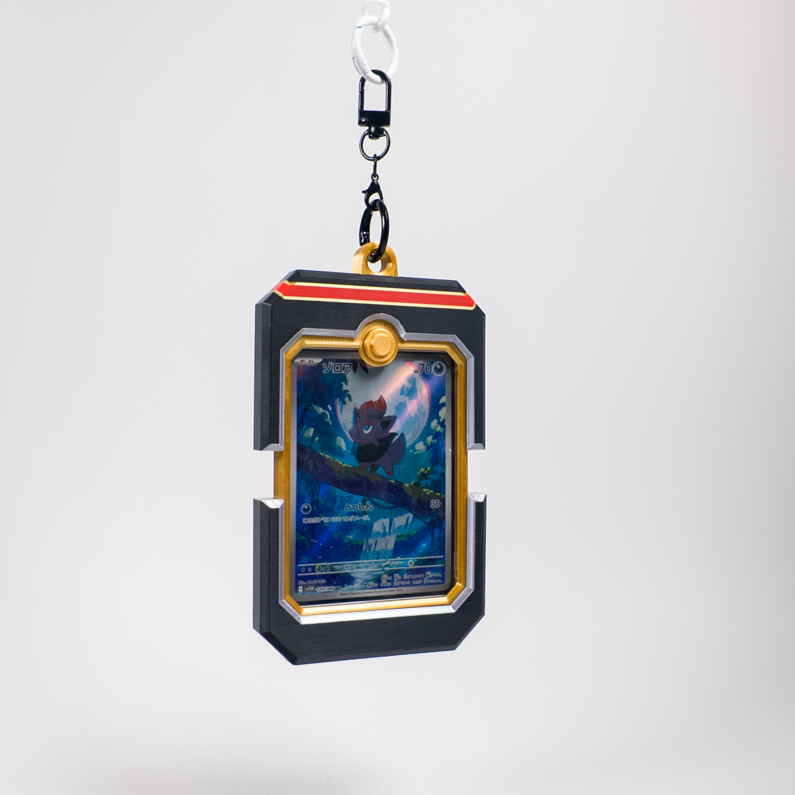 A collectible Pokémon TCG card displayed inside a black and gold card holder keychain, suspended from a black plastic clip on a light gray background.