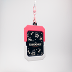 A pet ID tag keychain with a pink top section, a black middle section featuring a raccoon pattern and the text 'TANOOKIE', and a white bottom section, hanging from a pink clip against a light gray background.