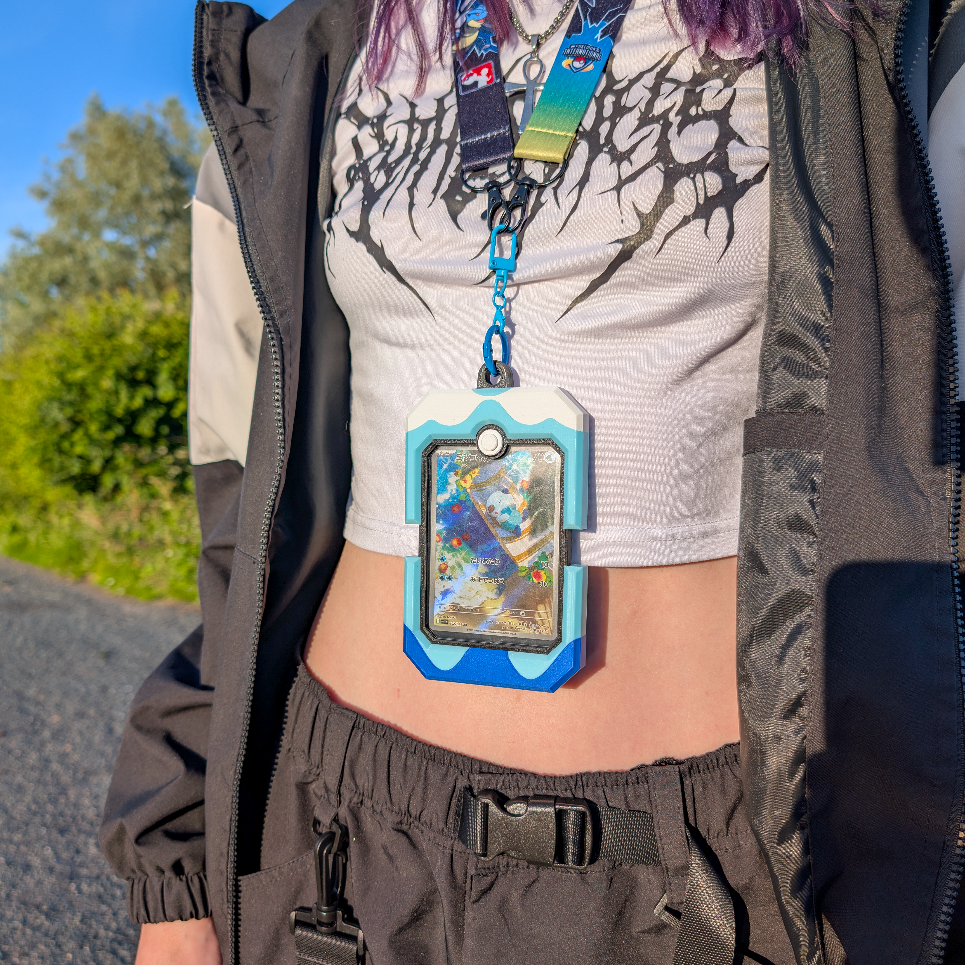 A close-up lifestyle shot of a person outdoors wearing a blue and white rugged phone pouch with a colorful screen protector, hanging from a lanyard around their neck over a white graphic crop top.