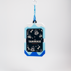 A dog ID tag keychain featuring a black center with white dog-themed illustrations and the text 'TANOOKIE' and 'TANOOKIES', surrounded by light blue and royal blue borders, suspended from a blue chain on a light gray background.